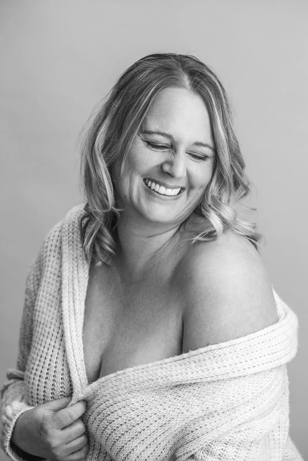 Selbstliebe im Boudoir-Portrait: lachende Frau im hellen Strickcardigan, Schwarzweiss