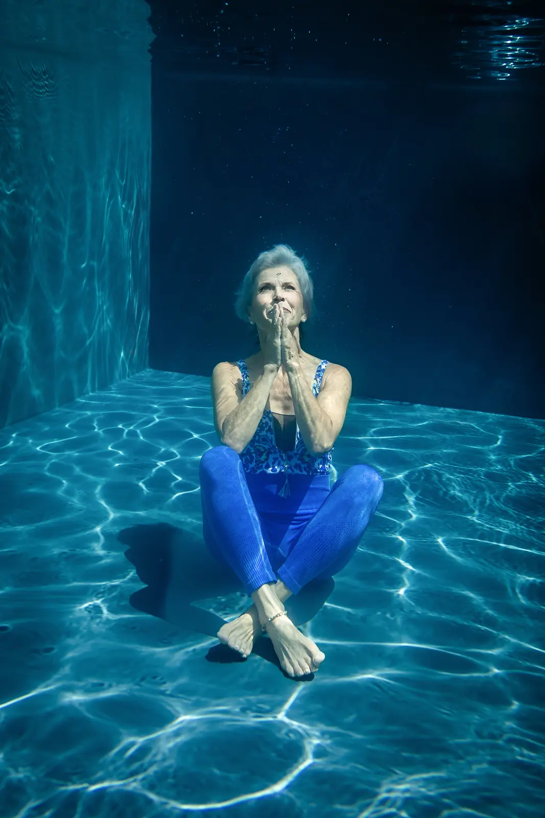 Yogalehrerin Monika meditiert unter Wasser auf dem Beckenboden, blaue Kleidung