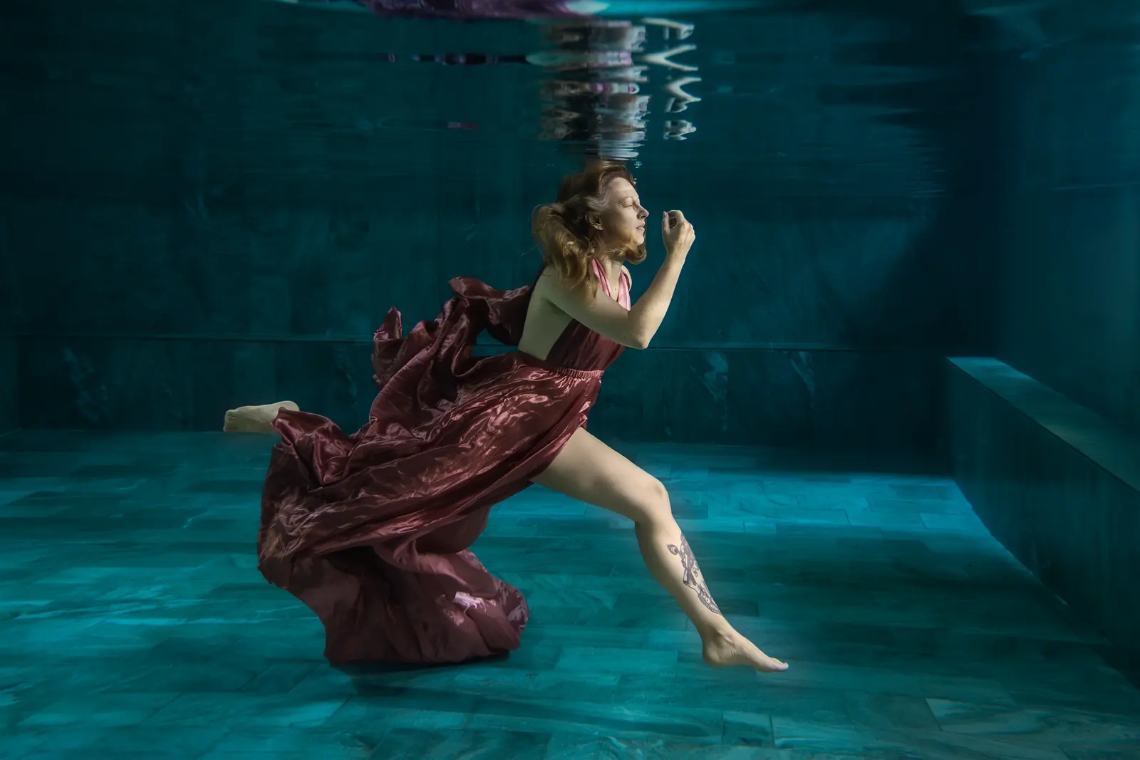 Frau im roséfarbenen Kleid macht unter Wasser einen grossen Schritt, Stoff fliesst hinter ihr